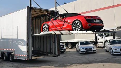 Red convertible loaded on a hydraulic lift gate into an enclosed car trailer