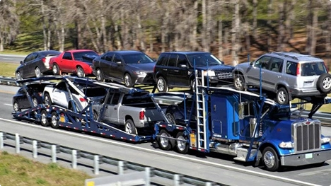 Blue semi car hauler transporting SUVs and sedans on a double deck open trailer on the highway