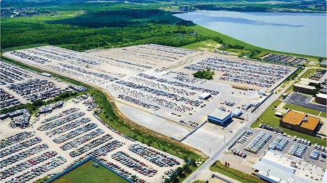 Aerial view of a large auto auction yard with rows of parked vehicles near a lake