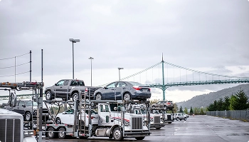 Multiple open car carriers parked near a suspension bridge on an overcast day