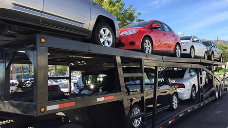 Double deck open car carrier loaded with sedans in a parking lot under blue sky