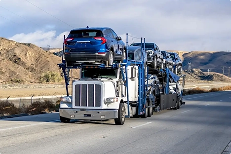 Open car hauler with multiple vehicles driving on a highway through desert hills