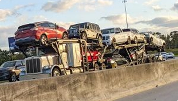 Loaded open car carrier driving on a busy highway beside a concrete divider