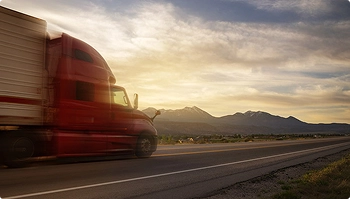 Red semi truck driving on a highway with mountains and sunset in background