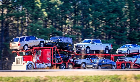 red car carrier trailer transporting multiple vehicles on highway