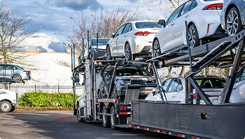open car carrier loaded with sedans near trees ready for dealer transport