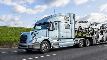 silver semi truck with car hauler driving on highway with loaded vehicles