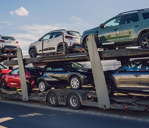open car carrier loading mixed SUVs and sedans on a city street