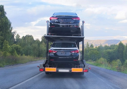 car carrier trailer transporting vehicles on a forest highway during daytime