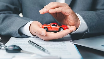 hands protecting small red sports car over paperwork symbolizing insured transport