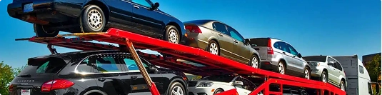 row of sedans on red open car carrier under clear blue sky for affordable car shipping