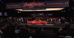 classic car on auction stage under spotlights with audience in dark venue