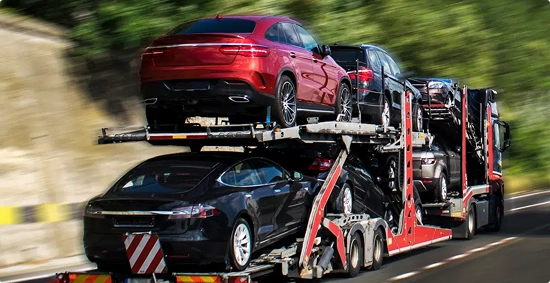 open car carrier transporting sedans and SUVs on a highway curve