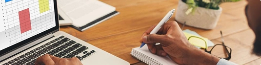 person analyzing transport cost data on laptop and writing notes for planning