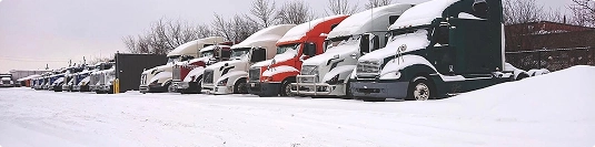 row of semitrucks parked in snow showing winter car shipping conditions