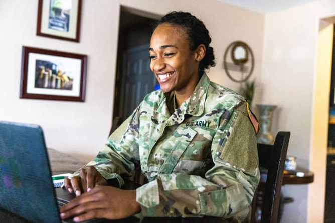female military service member smiling while using a laptop at home