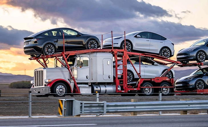 car hauler loaded with multiple vehicles driving on highway at sunset