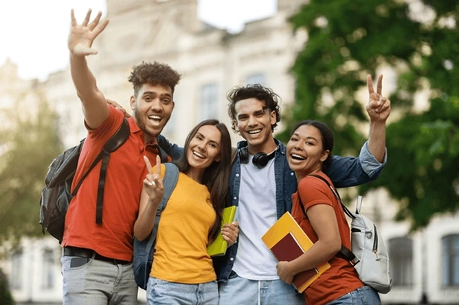 group of college students smiling outdoors holding books and backpacks