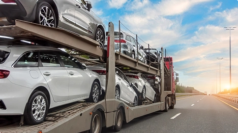 open car carrier transporting multiple vehicles on the highway at sunset