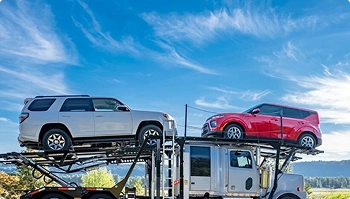 open car carrier transporting an suv and a compact car under blue sky