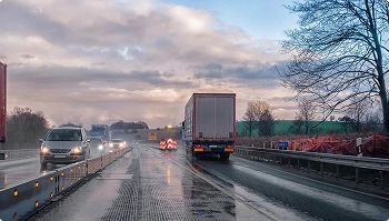 rainy highway with trucks and road work barriers causing weather delays