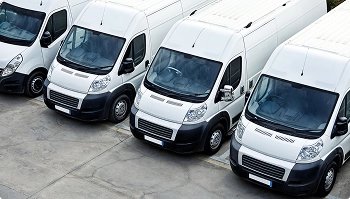 Row of white cargo vans parked in an industrial lot for fleet service
