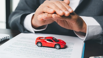 hands covering small red sports car over paperwork symbolizing insured transport protection