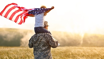 service member carrying child with us flag in a field at sunset symbolizing pcs support