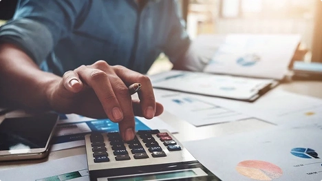 person using calculator with documents and charts on desk