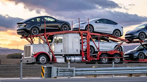 open transport truck carrying electric vehicles during sunset drive