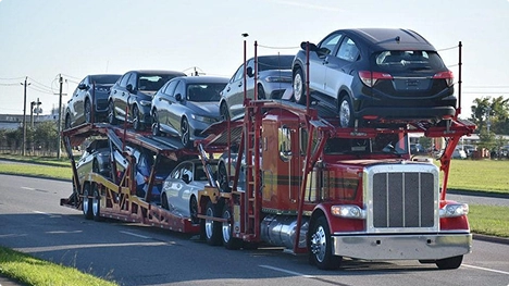 open car carrier hauling multiple vehicles on a suburban road