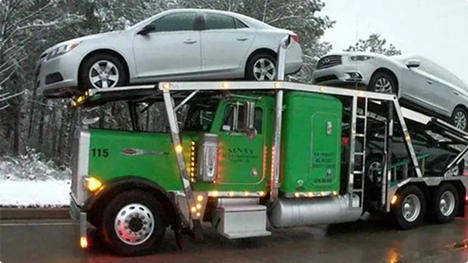 green open car carrier hauling sedans in snowy weather showing snowbird car shipping and winter ready transports