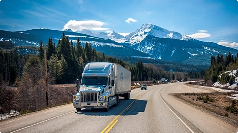 semi truck driving on a scenic mountain highway in clear weather symbolizing long distance auto transport