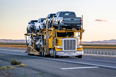 yellow open car carrier hauling pickup trucks on highway at sunset showing door to door auto transport