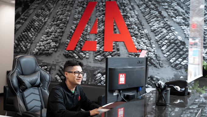 Employee working at a customer service desk inside an IAA auto auction office with vehicle yard imagery in the background