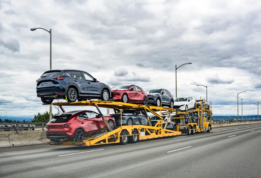 Open auto carrier hauling multiple passenger vehicles on a highway under cloudy sky conditions