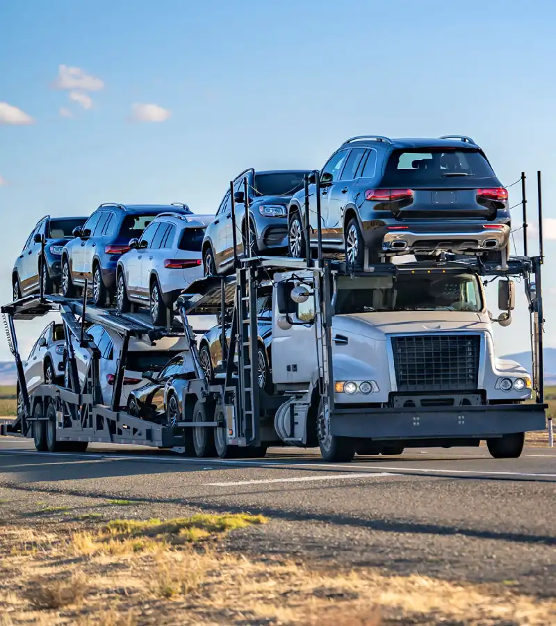 Open car carrier truck transporting multiple SUVs and cars on a highway during clear daylight conditions