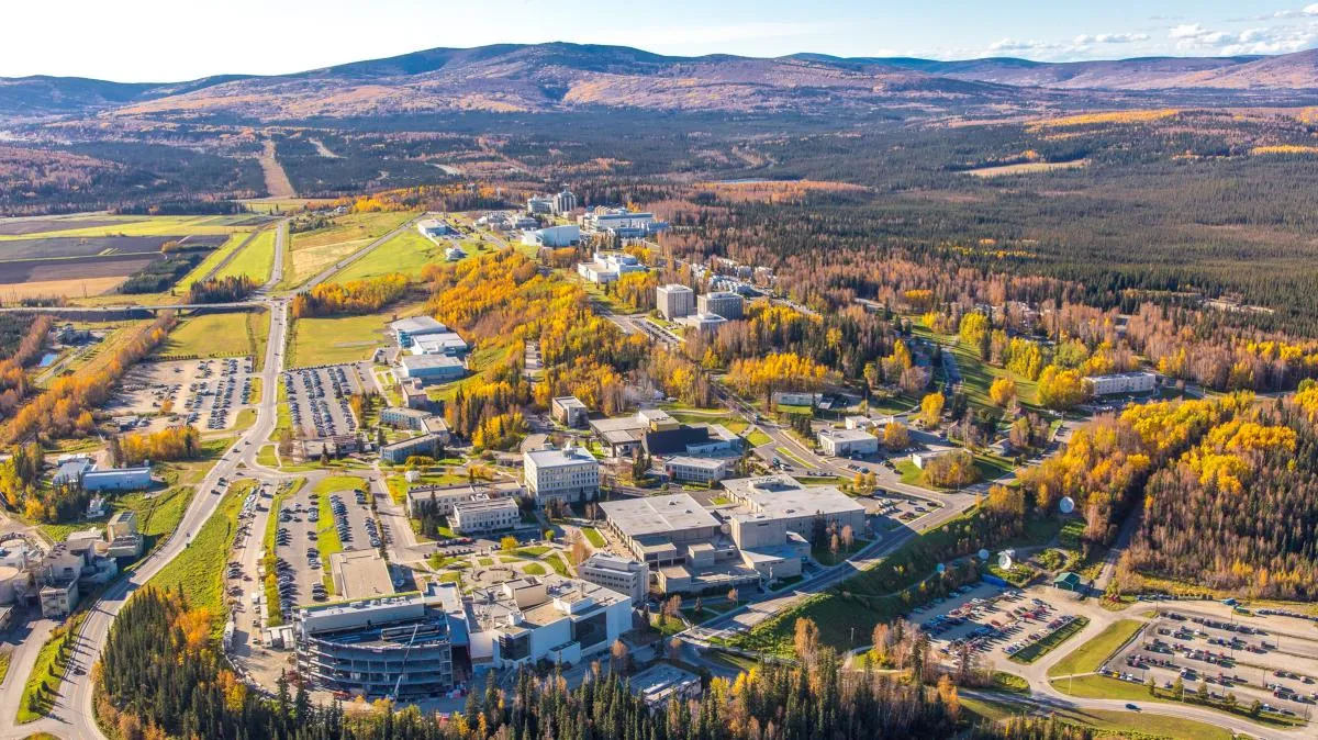 Aerial view of a large campus complex surrounded by autumn colored forests, roads, and rolling mountain landscape in daylight