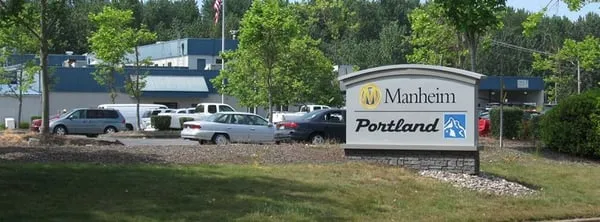 Entrance sign for Manheim Portland auto auction facility with parked vehicles and buildings in the background