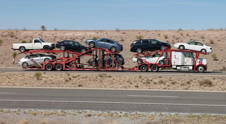 Open car carrier transporting multiple vehicles across a desert highway under clear daytime conditions