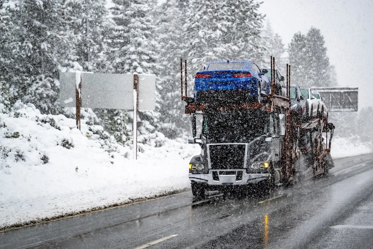 Open car carrier transporting multiple vehicles on a snowy highway during active winter conditions