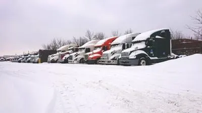 Row of semi trucks parked in a snow covered lot during winter weather conditions