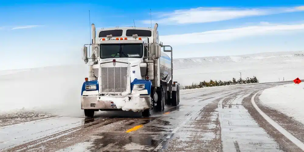 Semi truck driving on an icy winter road with snow buildup and cold weather conditions