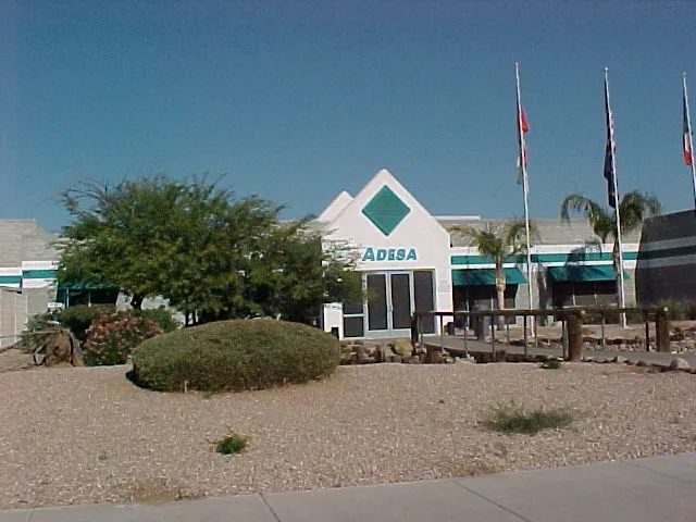 Exterior view of an ADESA auto auction facility with entrance signage, flags, and desert landscaping in daylight