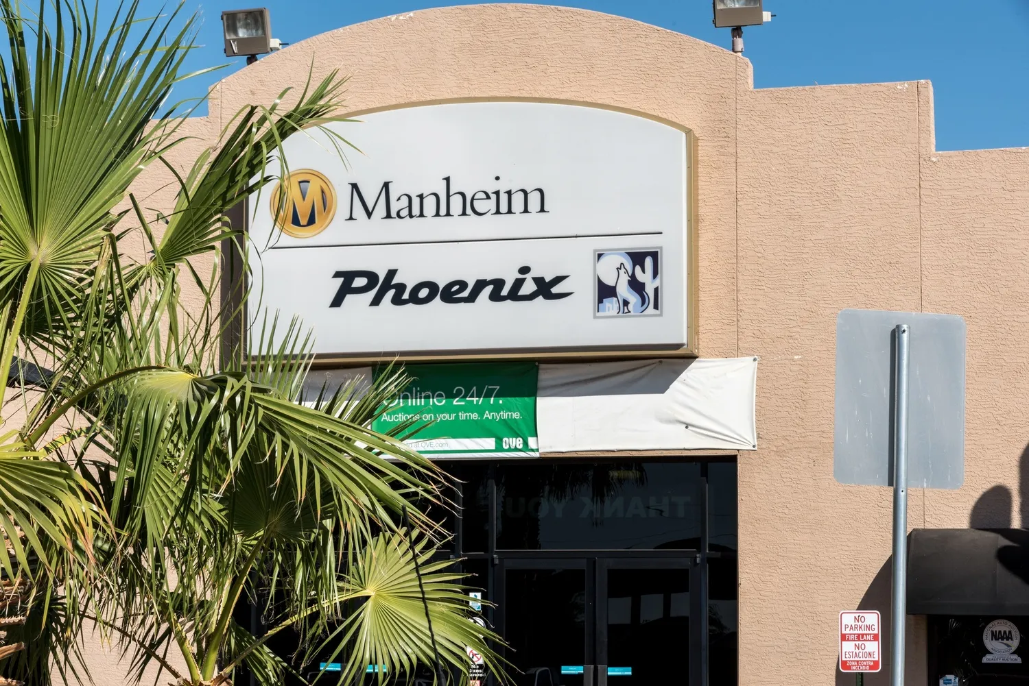 Entrance sign for Manheim Phoenix auto auction facility with palm trees and building facade in daylight