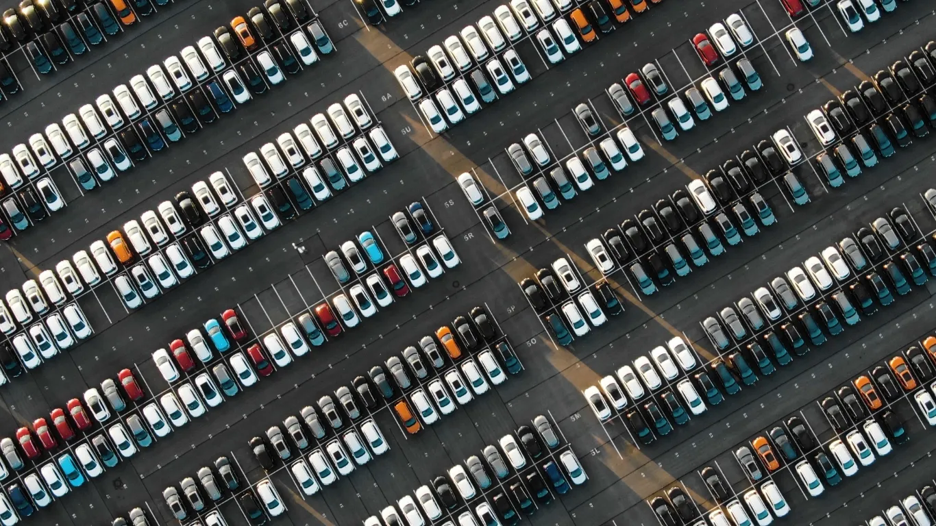 Aerial view of a large vehicle storage lot with rows of parked cars arranged in an organized pattern