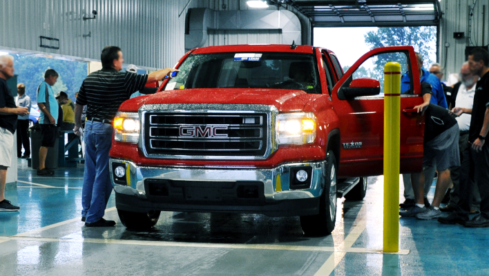 Red GMC pickup truck being inspected by buyers inside an indoor auto auction facility