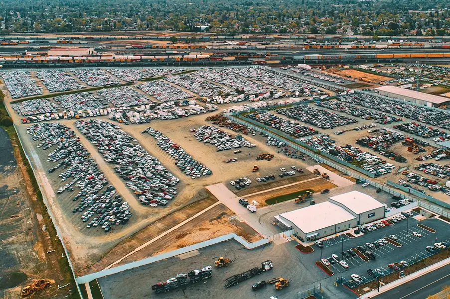 Aerial view of a large auto auction yard with thousands of vehicles parked in rows near rail lines and warehouses
