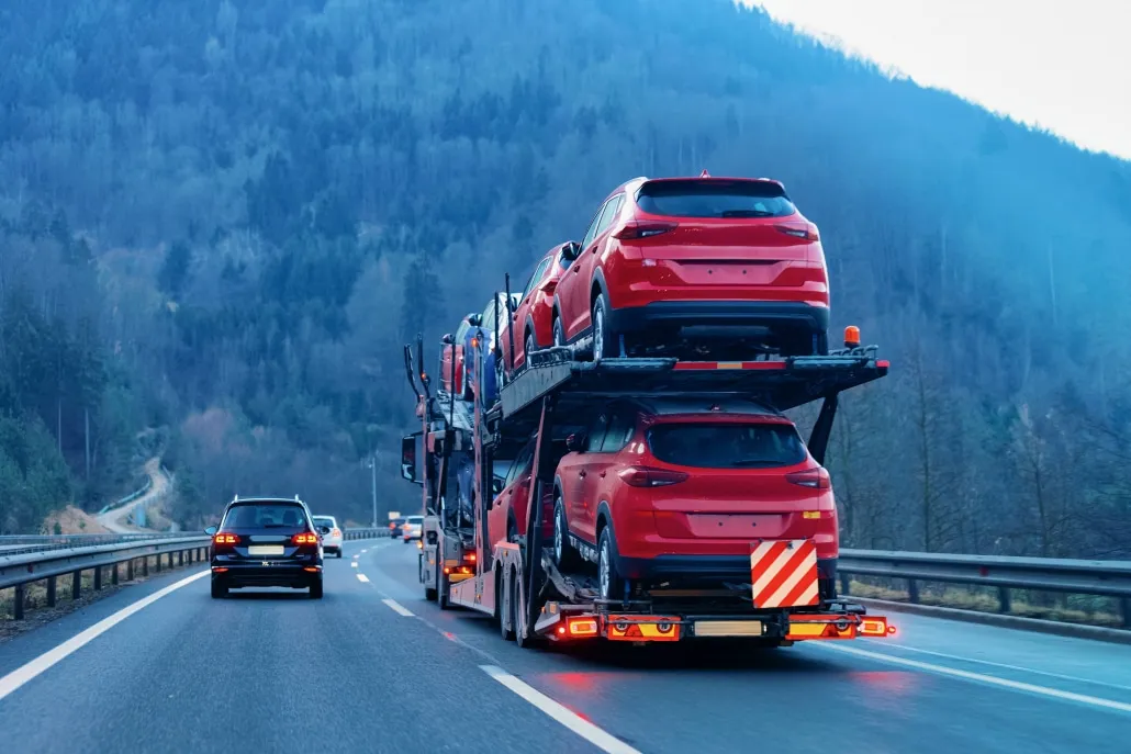 open car carrier transporting vehicles on mountain highway during long distance auto transport