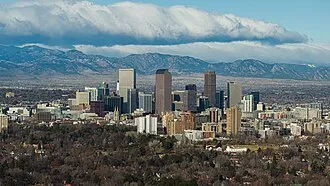 Denver skyline with downtown buildings and the Rocky Mountains visible in the background under a cloudy sky